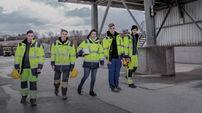 Five young people in bright yellow work clothes on a construction site