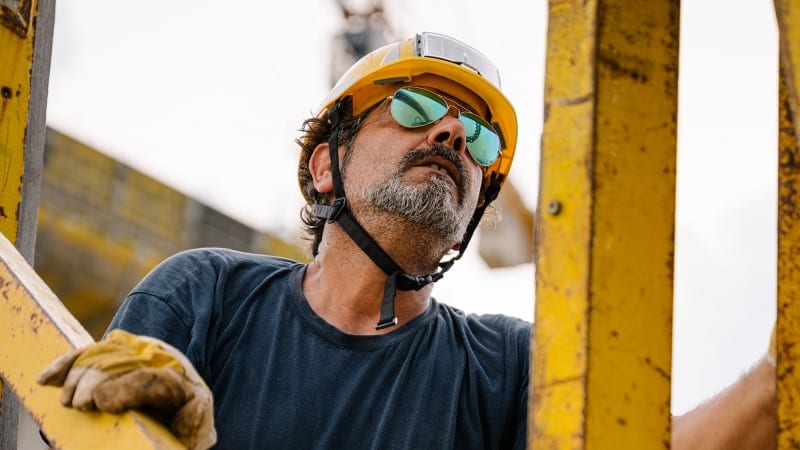 Etwa 50jähriger Mann mit Bauhelm, Bart und Sonnenbrillen bei der Arbeit