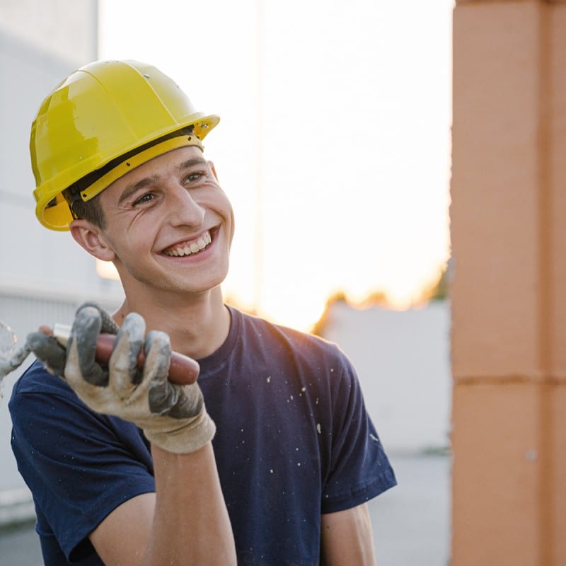 Young smiling man with construction helmet plastering on a construction site