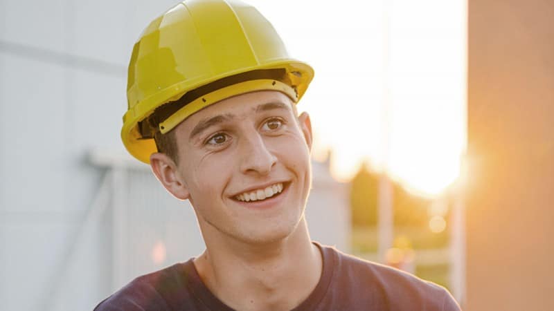 Junger lachender Mann mit Bauhelm bei Verputzarbeiten auf der Baustelle