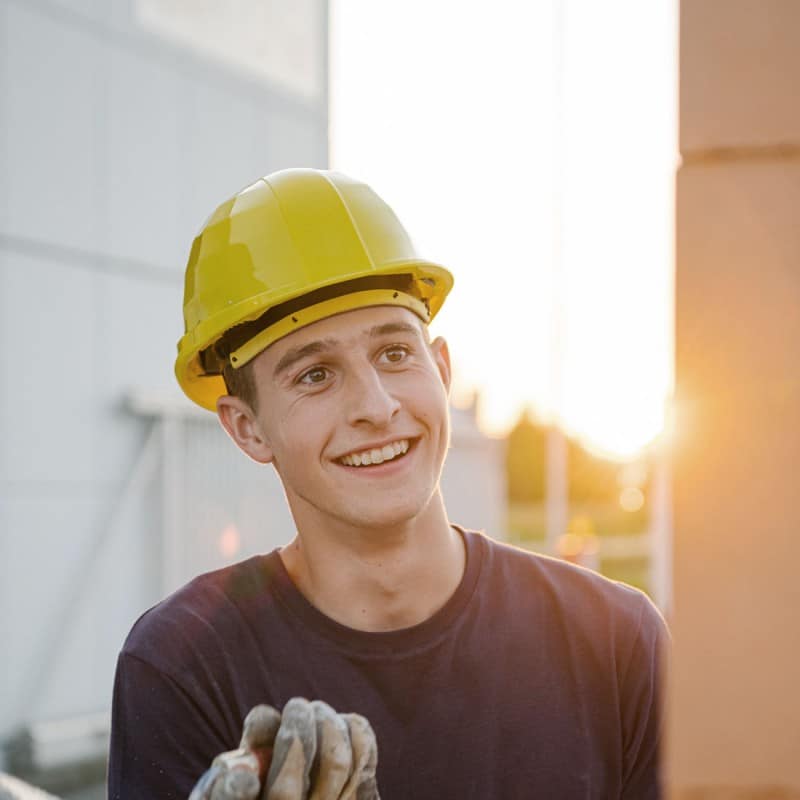 Junger lachender Mann mit Bauhelm bei Verputzarbeiten auf der Baustelle