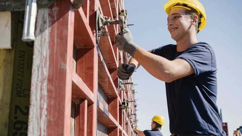 Junger Mann mit Bauhelm arbeitet an Betonrohbau © Joel Kernasenko Junger Mann mit Bauhelm arbeitet an Betonrohbau